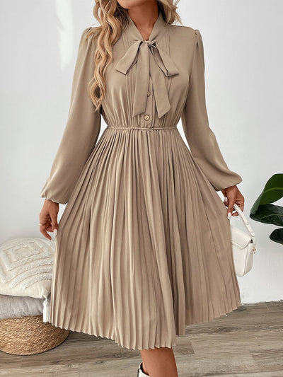 Perfee Pleated Tie Neck Long Sleeve Dress in beige, featuring a pleated design and tie neck detail.