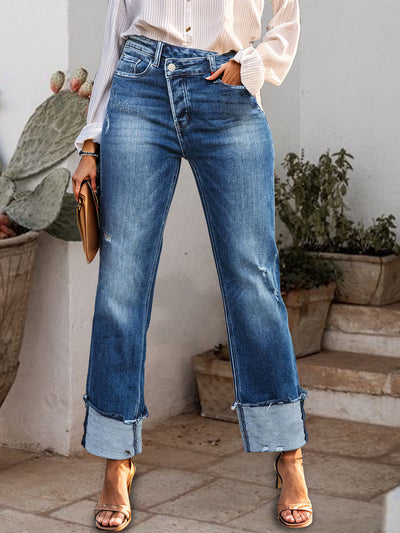 Stepped waist raw hem rolled straight jeans with buttoned feature displayed in an outdoor setting.