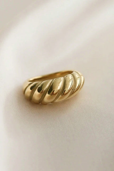 Gold twisted ring made of titanium steel with a shiny finish on a soft background.